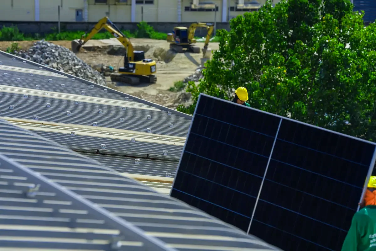 Operarios colocando grandes paneles solares sobre la cubierta de una nave industrial, energía solar para empresas en Toledo