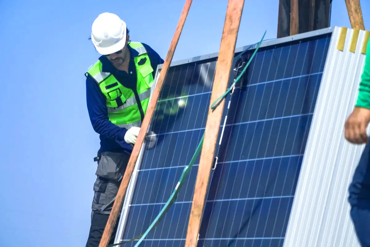 Instalador con casco y chaleco reflectante manipulando un panel solar durante un montaje de paneles solares en Toledo